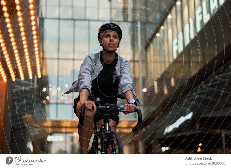 Frau Kurier Radfahren in der Nähe von hohen Gebäude mit Glasfenstern in der Stadt Radfahrer gemauert Großstadt Tag jung Sport Reiten Sommer Schutzhelm schützend