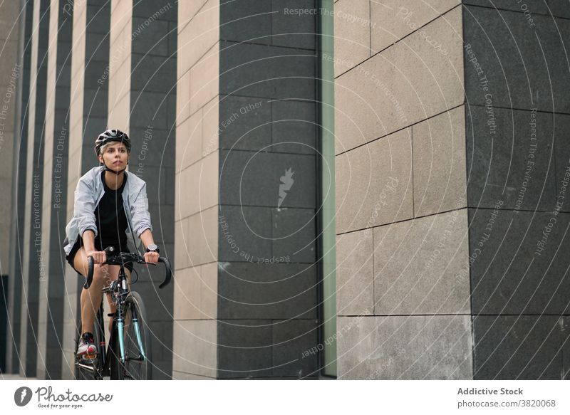 Weiblicher Kurier radelt in der Nähe eines hohen Gebäudes in der Stadt an einem Sommertag Radfahrer gemauert Großstadt Tag Frau jung Sport Reiten Schutzhelm