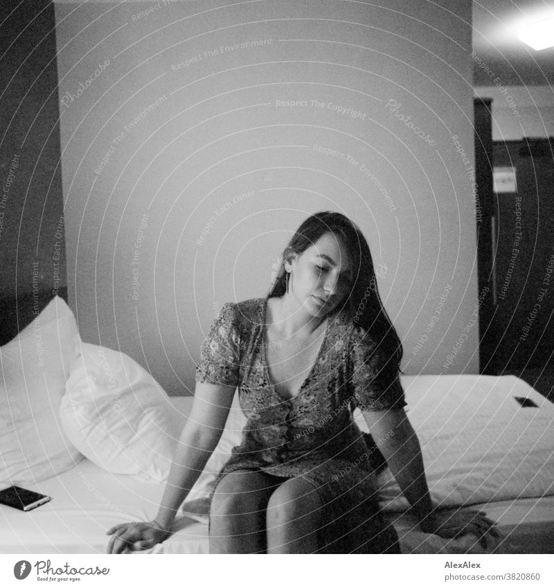 Portrait einer jungen Frau, die auf einem Hotelbett sitzt und nach unten schaut klassisch wild Sommerkleid Kleid Dekolleté Jugendliche Raum Zimmer