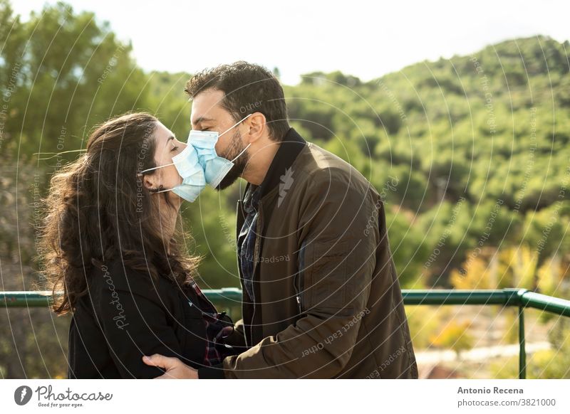Pärchenküsse im Freien mit einer chirurgischen Maske. Porträt im Freien als Symbol der pandemischen Liebe Paar Kuss Valentinsgruß covid-19 Mundschutz