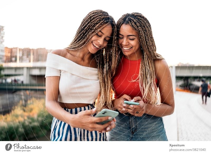 Glückliche Schwestern telefonieren per Telefon Tippen Lächeln Vorderansicht Afroamerikaner Zopf Straße attraktiv jung Stil Ausdruck schön hübsch ethnisch