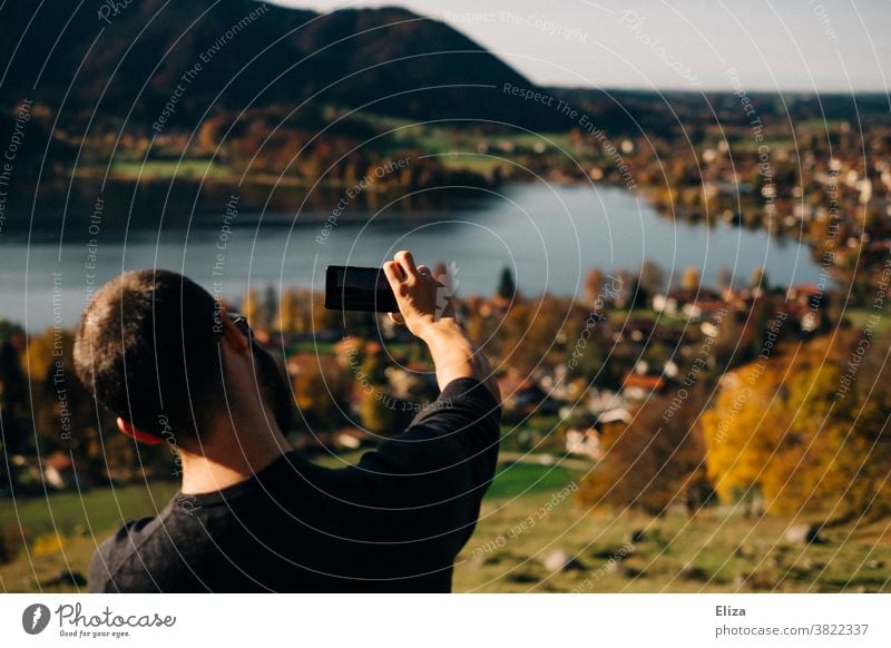 Ein Mann macht ein Foto mit seinem Handy vom Schliersee bei Sonnenschein landschaft See Smartphone fotografieren Ausflug Herbst Telefon Bayern Tourist Natur