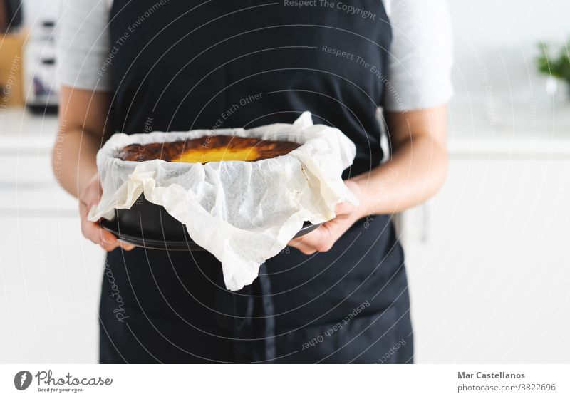 Frau in schwarzer Schürze zeigt einen Käsekuchen. Textfreiraum Murmel Kuchen Raum Küchenchef Koch Hände Dessert süß lecker Papier Gebäck gebacken verbrannt