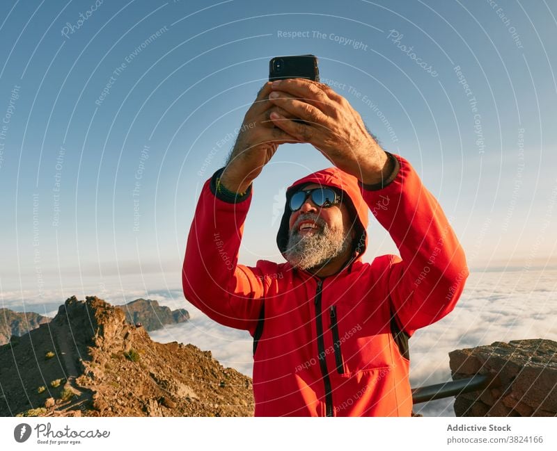 Fröhliche ältere Reisende nehmen Selfie in den Bergen Reisender Berge u. Gebirge Mann erkunden Wanderer Bergsteiger Smartphone Senior männlich Oberbekleidung