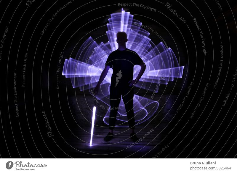 Silhouette eines mit einem Lichtschwert stehenden Mannes mit Neonzeichnungen und Leds bei der Lichtmalerei. säbeln abstrakt Kunst Junge hell Energie Kurve