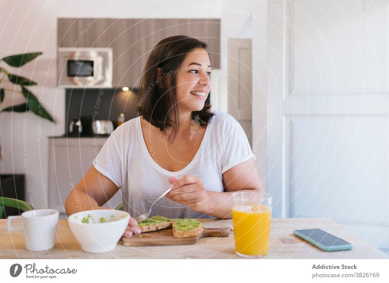 Lächelnde Frau, die beim Frühstück zum Fenster schaut im Innenbereich heimwärts Haus Mädchen Avocado kaufen Küche Kaffee Morgen Kaukasier brünett Tisch