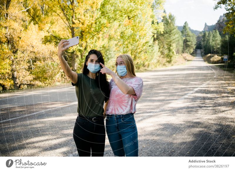 Junge Frauen in medizinischen Masken nehmen Selfie auf dem Lande Freund Mundschutz Coronavirus Straße Wald Smartphone Glück Freundschaft Telefon Mobile