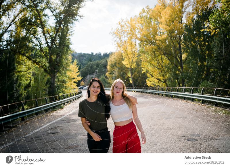 Glückliche Freundinnen umarmen sich auf der Landstraße Frauen Straße Wald Umarmung Herbst Freundschaft Landschaft Natur heiter jung Fahrbahn Zusammensein