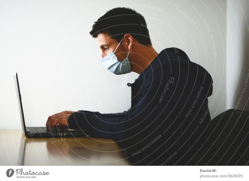 Quarantäne und Homeoffice - Mann arbeitet mit Atemschutzmaske am Laptop Corona Mundschutz alleine einsam Maske Corona-Virus Pandemie