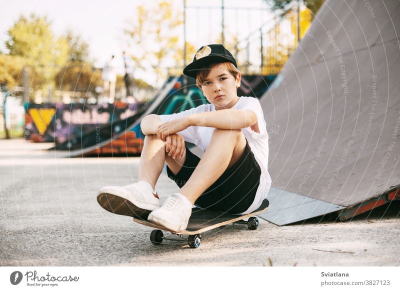 Ein wunderschöner Teenager sitzt auf einem Skateboard in einem speziellen Bereich des Parks. Ein Junge ruht sich nach einer Fahrt in einem Skatepark aus. Aktive Erholung an der frischen Luft