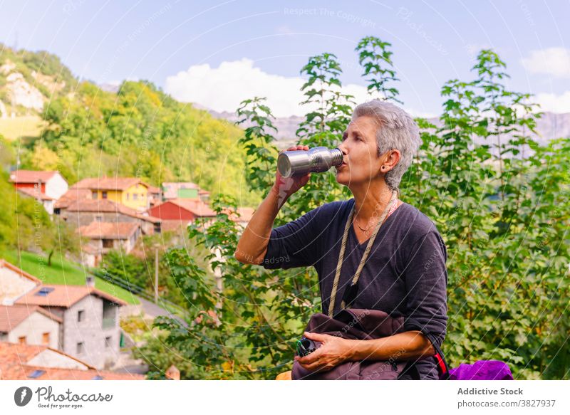 Reife weibliche Tourist trinken Tee aus Thermoskanne in der Nähe von Grün Berge Reisender Durst Berge u. Gebirge Natur Hochland Haus Frau Himmel wolkig