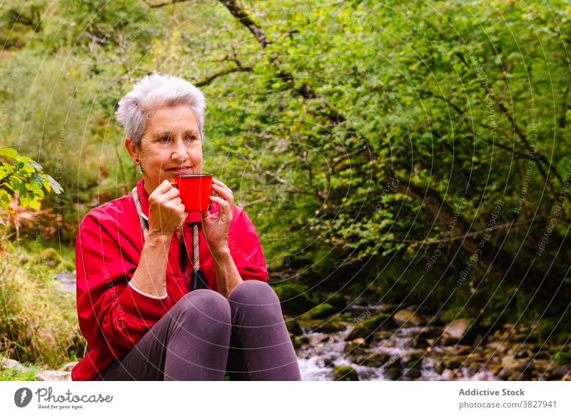 Älterer Reisender trinkt Wasser auf einem Stein in der Nähe eines seichten Flusses trinken Natur Fernweh reisen ruhen Frau Ausflug Durst sich[Akk] entspannen