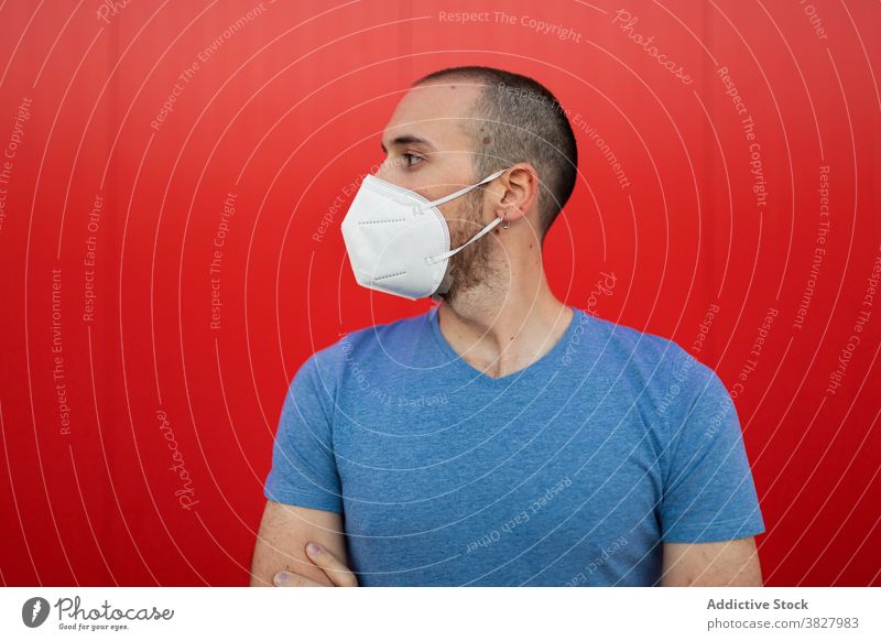 Männlich mit Maske in der Nähe der roten Wand in der Stadt Mann Mundschutz Atemwegserkrankungen COVID19 behüten neue Normale Selbstisolierung Großstadt Fokus