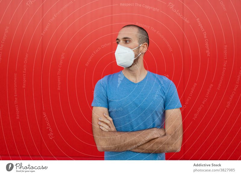 Männlich mit Maske in der Nähe der roten Wand in der Stadt Mann Mundschutz Atemwegserkrankungen COVID19 behüten neue Normale Selbstisolierung Großstadt Fokus