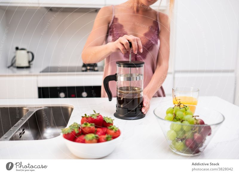 Crop Frau bereitet Kaffee zum Frühstück französische Presse Kaffeemaschine heimwärts Küche früh Pyjama vorbereiten Abfertigungsschalter Seide Getränk trinken