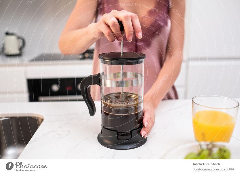 Crop Frau bereitet Kaffee zum Frühstück französische Presse Kaffeemaschine heimwärts Küche früh Pyjama vorbereiten Abfertigungsschalter Seide Getränk trinken