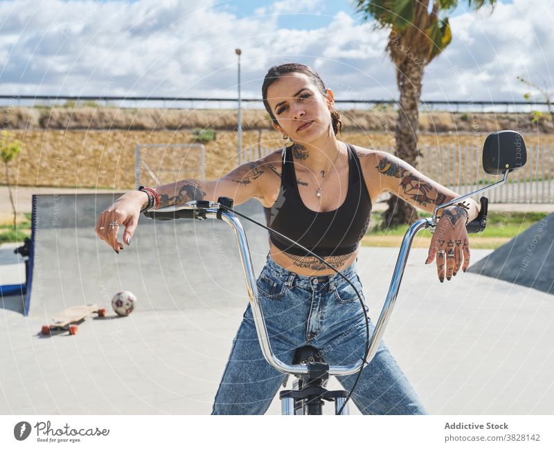 Ernste Frau auf dem Fahrrad im Skatepark bmx selbstbewusst Skateplatz extrem ernst Tattoo Stil Outfit sitzen trendy urban jung cool Verkehr Freiheit Sommer