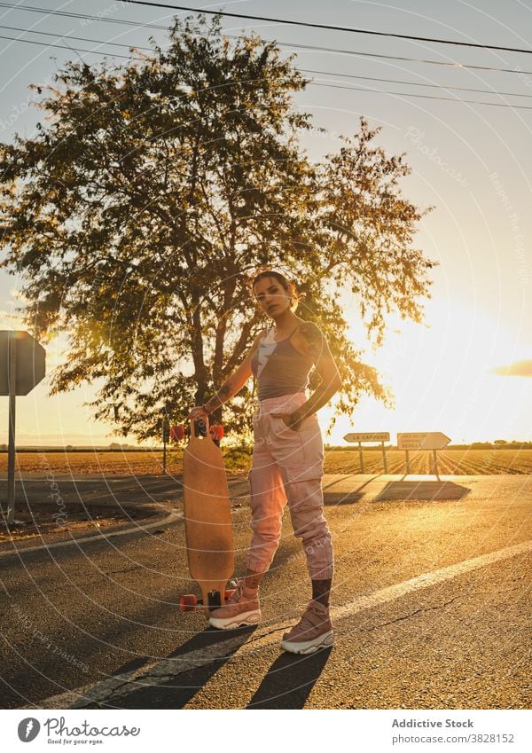 Selbstbewusste Frau mit Longboard auf der Straße Skater cool Stil Sonnenuntergang tausendjährig Individualität Sommer jung modern Hipster Zeitgenosse stehen