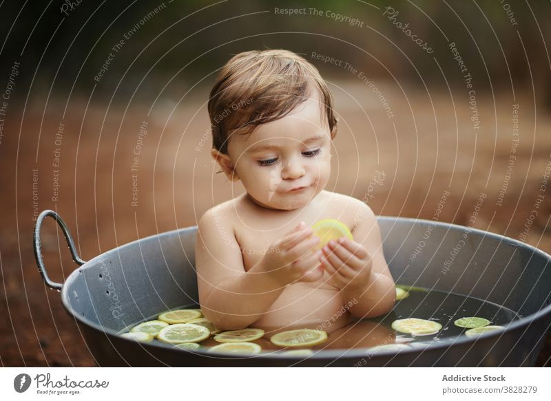 Adorable Kleinkind Kind essen Zitronen in Metall Bad Kindheit genießen nackt charmant unschuldig Baby Geburtstag feiern Sand Land Zitrusfrüchte Frucht Scheibe