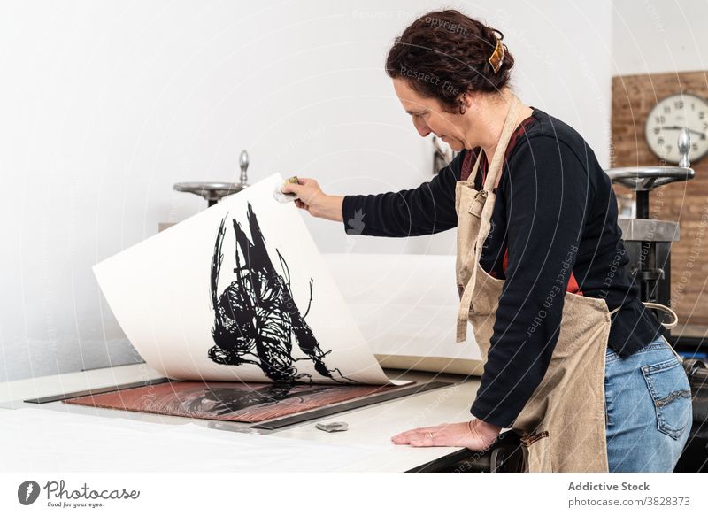 Druckgrafiker erstellt Linolschnittbild in der Werkstatt linocut drucken Presse Papier Eindruck kreieren Handwerk Kunstgewerbler Handwerkerin professionell