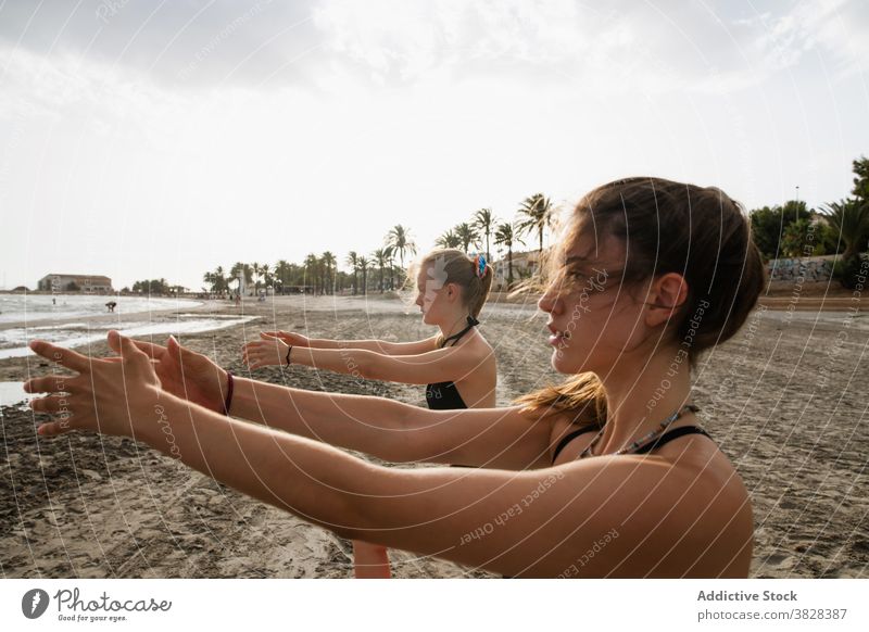 Konzentrierte Freunde üben Yoga an der frischen Seeluft Frauen Strand Windstille Achtsamkeit MEER Dehnung sandig Küste ausdehnen Fokus Handfläche wolkig Tag