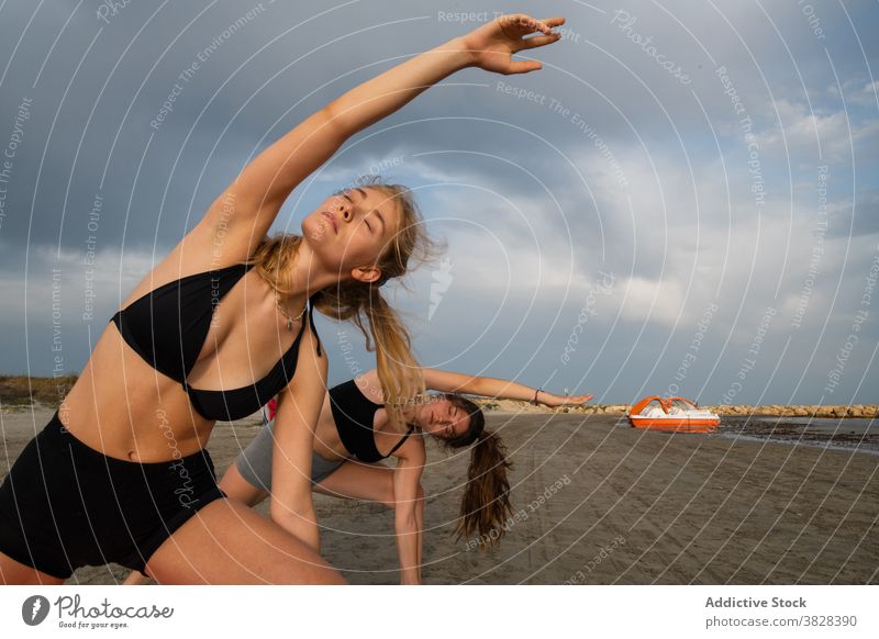 Junge Freunde machen Yoga am sonnigen Strand ernst beweglich üben sandig Küste kräuselnd Fluss trist Tag wolkig Gesundheit passen schlank Konzentration