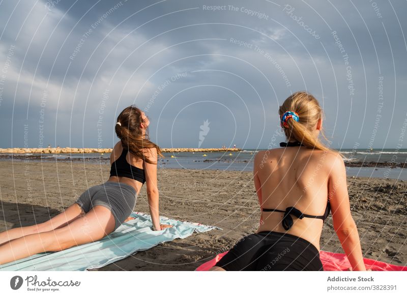 Junge Frauen liegen am Strand und tun Cobra Pose Yoga schlank Kobra-Pose ausführen beobachten Meer wellig schaumig bhujangasana Freiheit Erholung Sommer