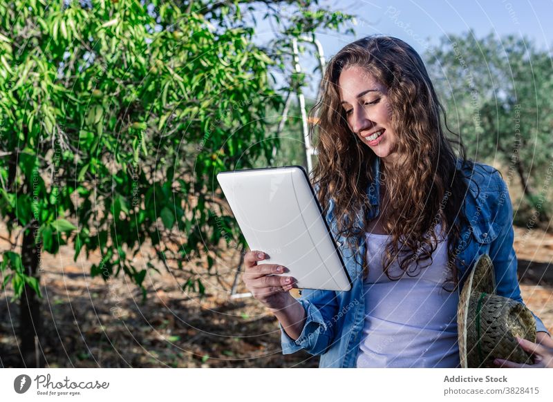 Junge Frau blättert Tablette stehend im Garten benutzend positiv Arbeit Obstgarten Ernte Frucht Bauernhof Browsen Anschluss digital professionell froh Gerät