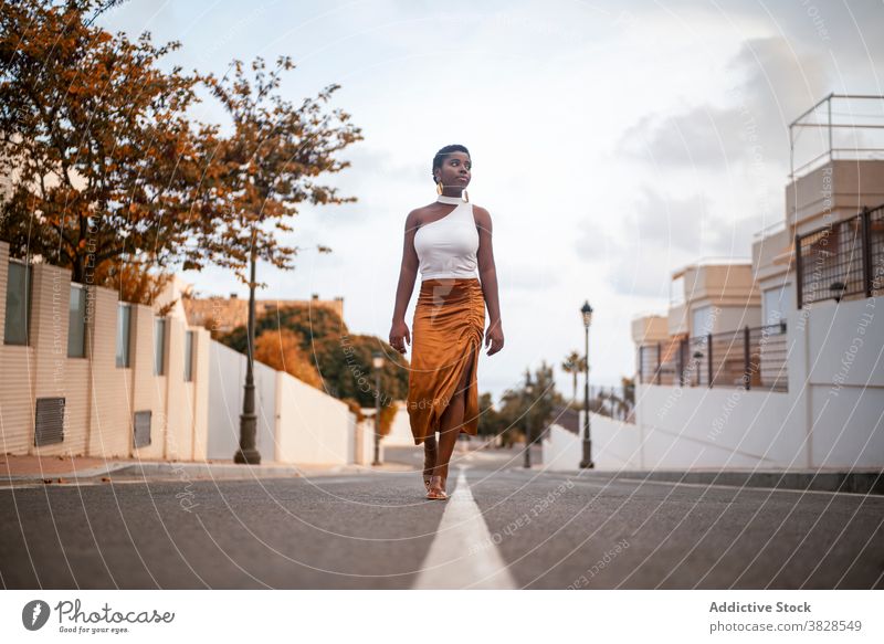 Stilvolle schwarze Frau zu Fuß auf Stadt Straße Spaziergang stylisch Bekleidung verträumt Aussehen Gebäude Großstadt tropisch Ohrringe nachdenken Natur Himmel