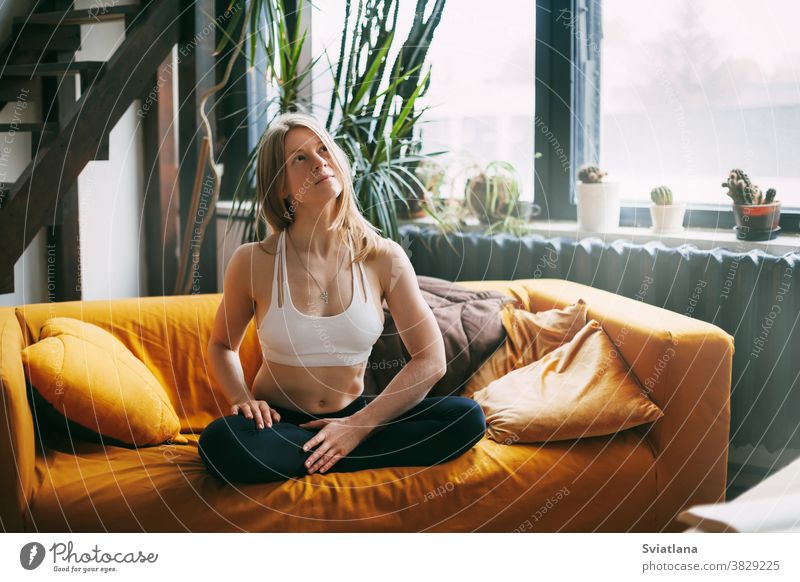 Gelassenes, ruhiges Mädchen, das in der Lotus-Position auf dem Sofa sitzt und zu Hause Yoga-Übungen zur Entspannung macht. Das Konzept des Seelenfriedens Frau