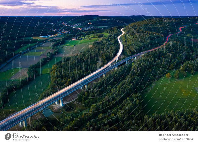 Luftaufnahme der Autobahn, die sich am Herbstabend über einen Waldhügel spaltet, lange Exposition oben Antenne Ackerbau Architektur blau Brücke Wolken
