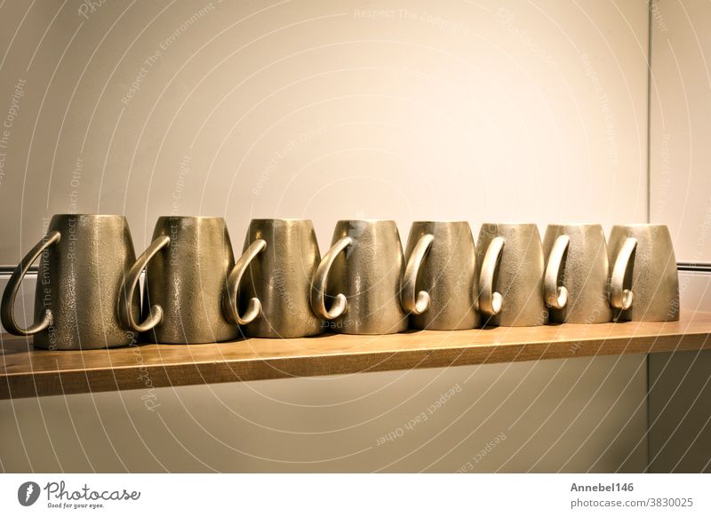 gold- oder kupferfarbene Tassen auf Holzregal in einer Reihe in der Küche. Kaffee- oder Teetasse im Retro-Design trinken Regal schön weiß Porzellan Café Wand