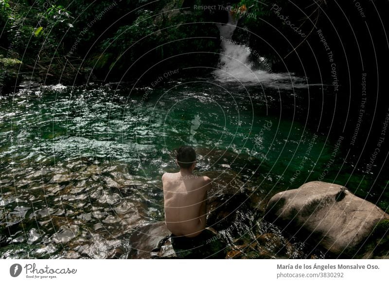Ein Mann sitzt auf einem Felsen vor einem grünen Wasserbrunnen eines Flusses im Dschungel. Lifestyle Naturschutzgebiet Naturpark Naturliebhaber Naturfotografie
