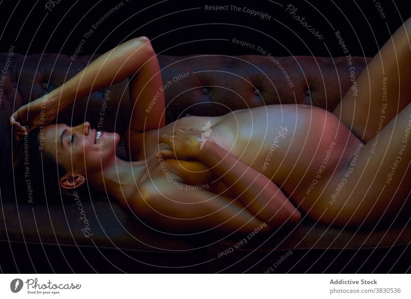 Sinnliche schwangere Frau auf dem Sofa liegend in der Dunkelheit Bauch erotisch Mutterschaft Lächeln vorwegnehmen erwarten heiß sexy nackt Elternschaft
