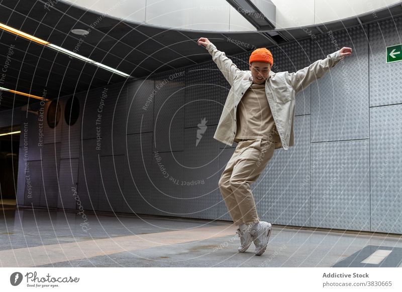 Fröhlicher asiatischer Mann steht auf Zehenspitzen im Gebäudeflur Körperhaltung Glück Tanzen heiter ausdehnen Flur Bewegung dynamisch cool Stil aufgeregt