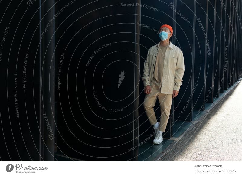 Emotionsloser asiatischer Mann mit Gesichtsmaske lehnt an einer Hauswand emotionslos Melancholie Mundschutz Gebäude Deckel Mund Pandemie Coronavirus