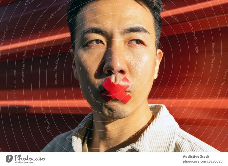 Crop Asiatischer Mann mit Klebeband auf Lippen Ruhe Siegel Stummheit Konzept stumm nachdenken nachdenklich stimmlos besinnlich Konzentration ernst ruhig