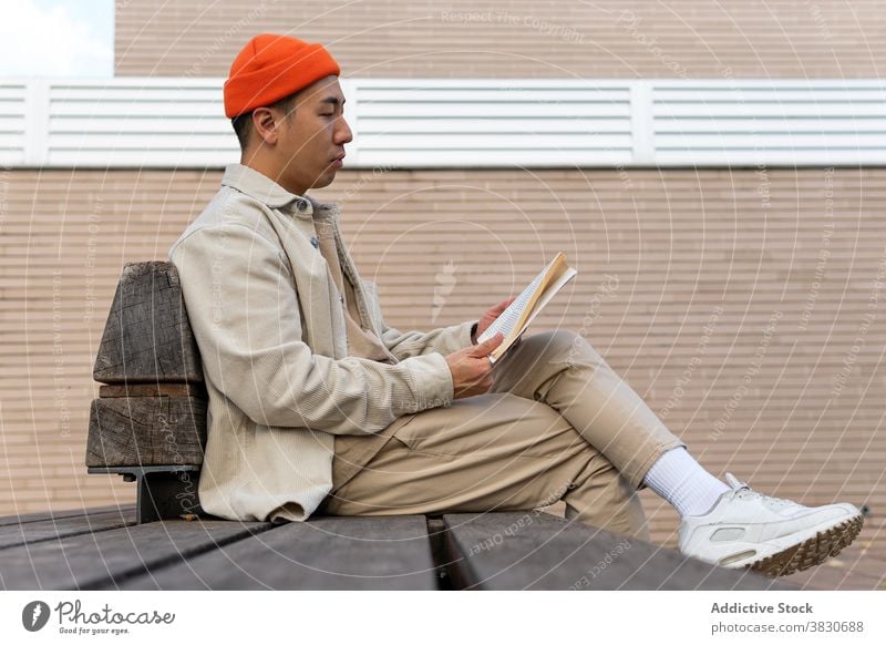 Konzentrierte asiatischen Mann Lesen Buch auf Straße Bank lesen Leseratte genießen Literatur Wissen Hobby Konzentration ernst Bildung Lifestyle Fokus lernen