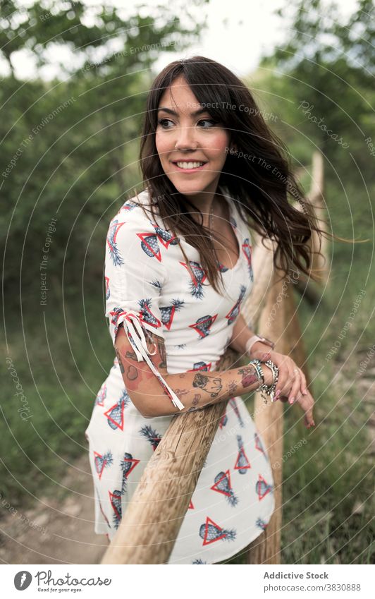 Verträumte Frau lehnt an Holzzaun auf Gehweg stehen Wald Park verträumt Stil Mode Natur Kleid Tattoo Zaun dunkles Haar Accessoire Vorschein nachdenken träumen