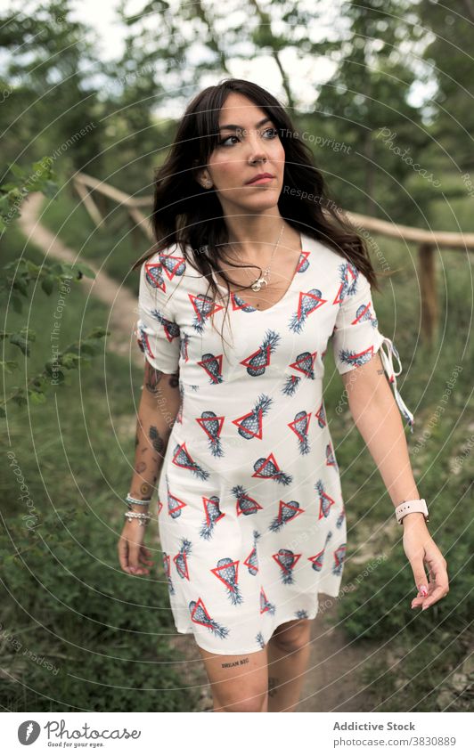 Verträumte Frau, die auf dem Fußweg am Zaun entlang geht Spaziergang nachdenklich schlendern Wald Park verträumt Stil Mode Natur Kleid Tattoo besinnlich ernst