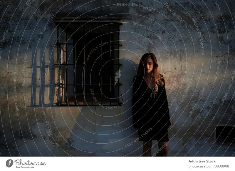 Frau in schwarzem Kleid steht in der Nähe verwitterten Gebäude schäbig Wand gealtert Grunge allein trist Depression jung Außenseite antik Haus Windstille ruhig