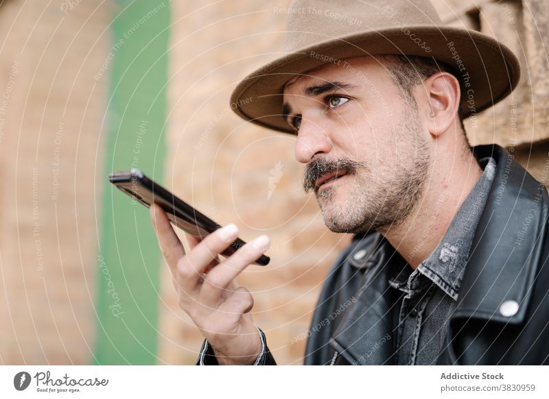 Nachdenklich nachdenklich trendigen Mann Aufnahme Nachricht auf Smartphone trendy Schnurrbart Stimme Aufzeichnen Mobile Vollbart Hut Lederjacke männlich Gebäude