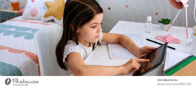 Mädchen lernt zu Hause mit Tablette und Maske auf dem Tisch studierend Schule zu Hause Heimunterricht Coronavirus covid-19 digitale Weisheit