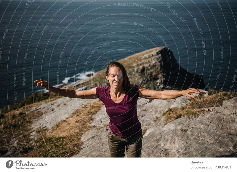 Frau hebt die Arme und tanzt an der Küste auf der Spitze einer Klippe, mit dem Meer im Hintergrund. Nizza inspirierend Waffen Küstenlinie Sightseeing Reisender