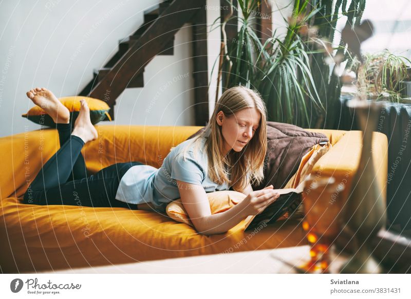 Eine junge Frau liegt auf dem Sofa und liest ein Lieblingsbuch. Das Mädchen ruht sich aus, widmet ihre freie Zeit dem Lesen. Buch lesen Glück lebend Roman