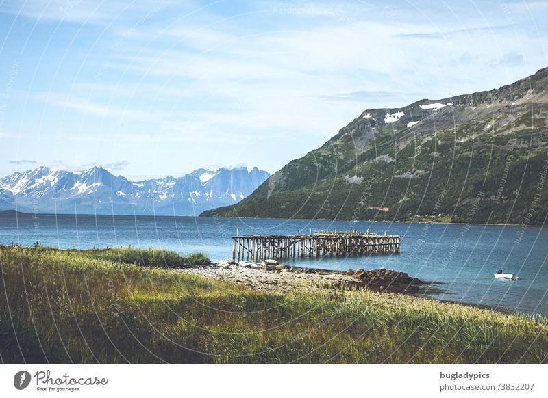 Fjordlandschaft in Norwegen mit einem Steg der ins Wasser führt, dem Blick auf den Fjord und Schneebedeckten Bergen im Hintergrund. Fjordausblick Landschaft