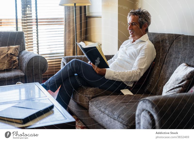 Reifer Mann liest Buch zu Hause lesen Sofa Tisch sitzen männlich lässig modern Lifestyle Fokus reif Erwachsener sich[Akk] entspannen ruhen klug Etage