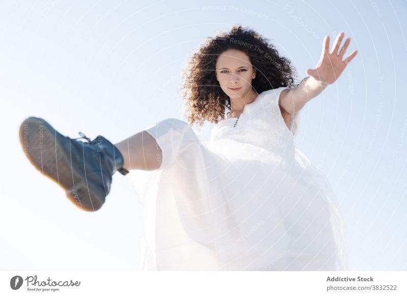 Fröhliche glückliche Frau springt und schaut in die Kamera auflehnen springen Freiheit cool ethnisch Dehnung weißes Kleid Sommer positiv jung heiter Spaß modern