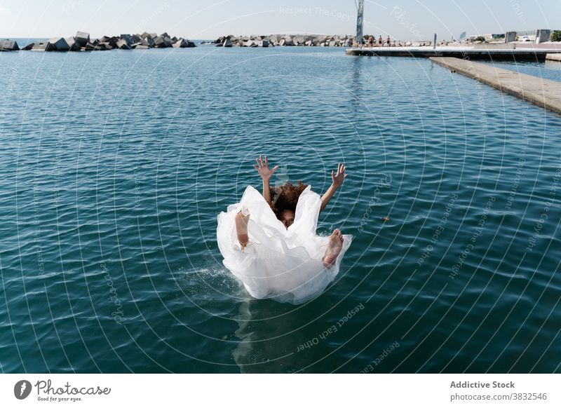 Anonyme Frau im Brautkleid fällt ins Wasser weißes Kleid hochzeitlich fallen Barfuß Strandpromenade See Pier jung aufgeregt ertrinken Spaß flippig Stauanlage