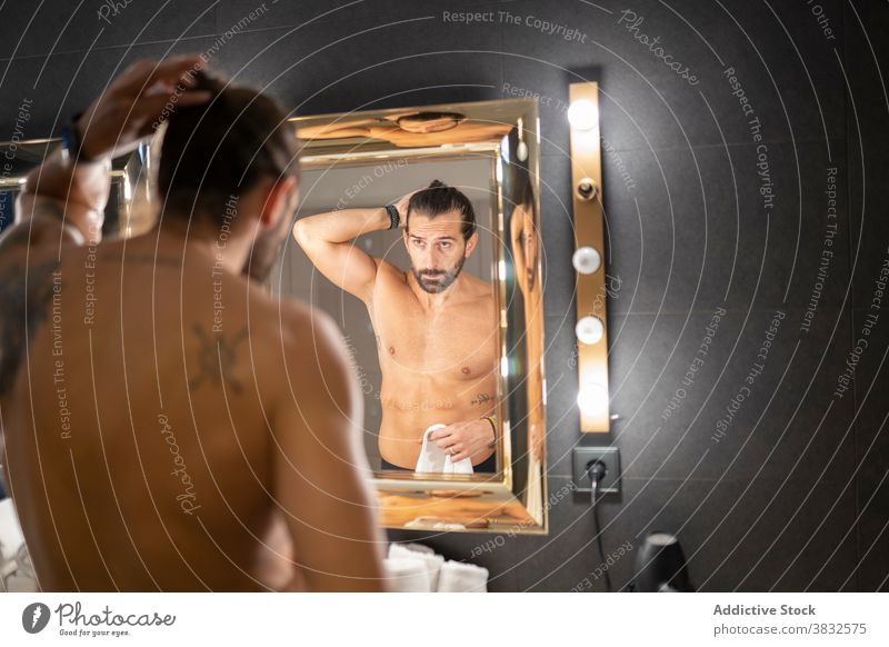 Shirtless Mann tun Haare in der Nähe von Spiegel Pferdeschwanz Bad Frisur modern leuchten Lampe ohne Hemd Reflexion & Spiegelung männlich Erwachsener Vollbart